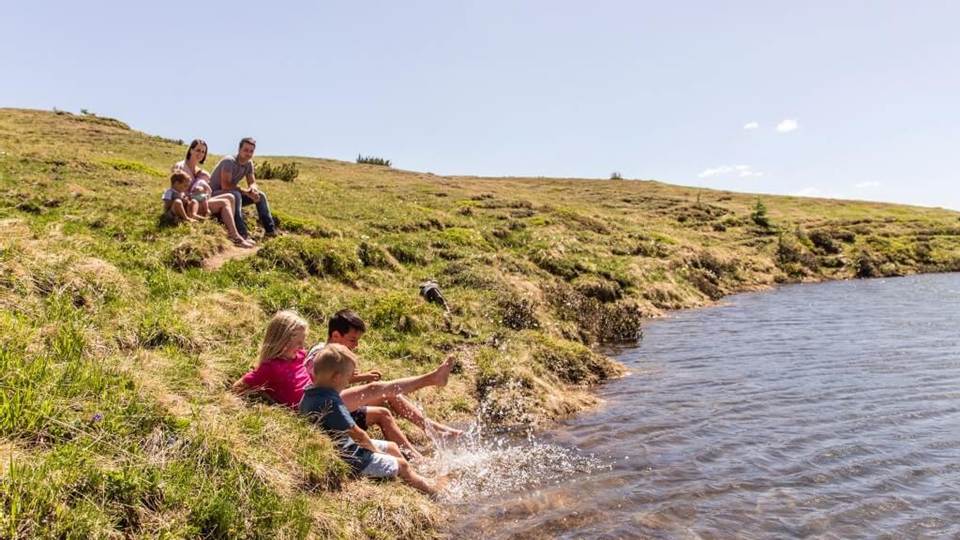 Familie sitzt am See während die Kinder ihre Füße in das Wasser halten